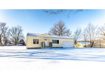 Charming yellow home with a large front yard covered in snow and attached garage at 5757 E 21St St, Indianapolis, IN 46218