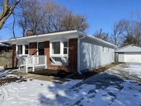 Charming single-story home featuring a brick facade, light blue siding, and a detached garage during winter at 2411 N Kitley Ave, Indianapolis, IN 46219