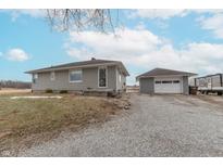 Charming single-story home featuring gray siding, a detached garage, and a gravel driveway at 12771 E 25Th St, Columbus, IN 47203