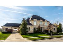 Stunning stone-clad home featuring a porte-cochere, manicured lawn, and beautiful mature trees at 1813 Milford St, Carmel, IN 46032