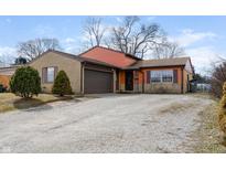 Charming split-level home featuring a brick and orange exterior, a gravel driveway, and an attached two-car garage at 3332 Ashway Dr, Indianapolis, IN 46224