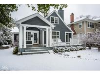 Charming gray home featuring a covered porch, white columns, and manicured landscaping dusted with snow at 5736 Central Ave, Indianapolis, IN 46220
