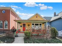 Charming yellow home features a cozy front porch, red door, and well-maintained landscaping at 645 E 9Th St, Indianapolis, IN 46202