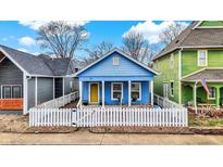 Charming blue home featuring a cozy front porch, bright yellow door, and white picket fence at 912 Harlan St, Indianapolis, IN 46203