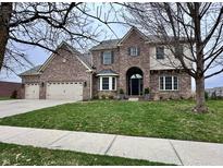 Traditional brick two-story home with arched entry, three-car garage, manicured lawn, and mature trees at 15050 Bainbridge Ct, Westfield, IN 46074