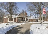 Charming brick home with a curved driveway, American flag, and mature trees in a snowy winter landscape at 3762 N Foxcliff E Dr, Martinsville, IN 46151