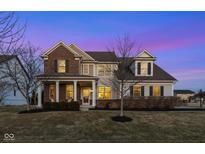 Beautiful two-story home featuring a welcoming front porch and manicured lawn at dusk at 10055 Win Star Way, Fishers, IN 46040