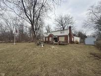 Charming two-story brick home with spacious front yard, surrounded by mature trees, complemented by an American flag at 6777 E Pleasant Run Pkwy S Dr, Indianapolis, IN 46219
