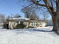 Charming one-story home with stone facade and attached garage, surrounded by a snow-covered yard and mature trees at 2104 W Barcelona Dr, Muncie, IN 47304