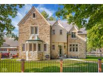 Charming stone home with a beautifully landscaped yard, framed by mature trees and a black metal fence at 906 Franklin St, Columbus, IN 47201