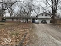 Ranch-style house with an attached garage and a gravel driveway, surrounded by leafless trees at 9550 N Delaware St, Indianapolis, IN 46240