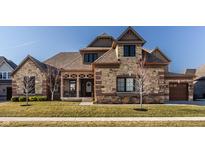 Charming exterior elevation with a stone and brick facade, covered porch, and well-manicured lawn at 4287 Prairie Falcon Dr, Zionsville, IN 46077