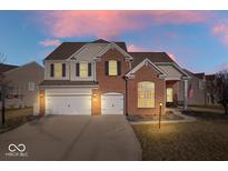 Charming two-story brick home featuring a three-car garage and well-manicured lawn at sunset at 348 Entrance Hall, Greenwood, IN 46142