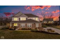Two-story home with a brick facade, manicured lawn, and a colorful sunset at 12073 Springtide Ln, Fishers, IN 46037