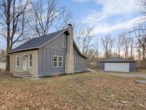 Charming gray home featuring stone accents, a classic chimney, and a detached garage, nestled among mature trees at 3905 N Drexel Ave, Indianapolis, IN 46226