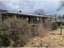 A view of a home's exterior with overgrown foliage obscuring the front, and a cloudy sky above at 4718 W 36Th St, Indianapolis, IN 46222