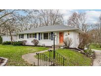 Charming one-story home featuring a white brick facade, blue shutters, and a vibrant orange front door at 6490 N Oxford St, Indianapolis, IN 46220