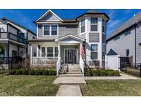 Charming two-story gray home boasts a welcoming front porch, well-manicured lawn, and a lovely American flag at 1820 Carrollton Ave, Indianapolis, IN 46202