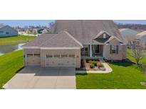 Beautiful brick home featuring a three-car garage, covered porch, and manicured lawn near a pond at 9559 Summer Hollow Dr, Fishers, IN 46037