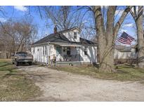 Charming one-story home with a welcoming front porch and American flag, set against a backdrop of mature trees at 3014 Alice Ave, Indianapolis, IN 46237