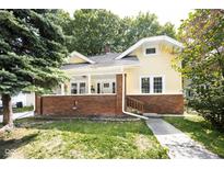 Charming yellow two-story home featuring a brick foundation, covered front porch, and well-maintained lawn at 415 Ruskin Pl, Indianapolis, IN 46205