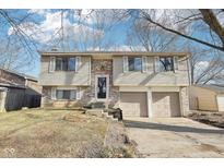 Split level home with tan siding and a brick facade features a two-car garage and a front yard at 5426 Sleet Dr, Indianapolis, IN 46237