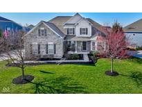 Charming two-story home featuring a manicured lawn and detailed brickwork and a front yard tree in full bloom at 13875 Ambria Dr, McCordsville, IN 46055