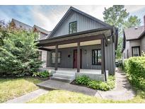 Charming home featuring a covered porch, gray siding, a red door, and lush landscaping at 615 E Morris St, Indianapolis, IN 46203
