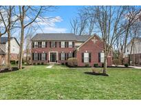 Traditional two-story red brick home featuring a lush front lawn, black shutters, and well-manicured landscaping at 6545 Briarwood Pl, Zionsville, IN 46077