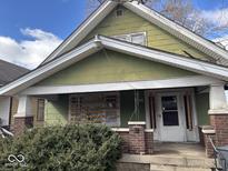 Olive green home exterior with covered porch and boarded window on a sunny day at 942 N Oxford St, Indianapolis, IN 46201