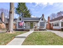 Charming cottage-style home featuring a manicured lawn, inviting walkway, and a cozy front porch with an American flag at 5937 Guilford Ave, Indianapolis, IN 46220
