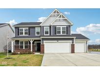 Charming two-story home featuring a three-car garage, brick accents, and blue siding against a partly cloudy sky at 8818 Tributary Dr, Indianapolis, IN 46259