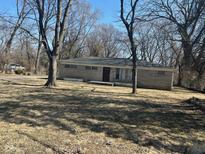 A single story home with a stone facade sits behind trees on a large front lawn at 3817 N Sheridan Ave, Indianapolis, IN 46226