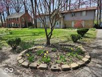 Landscaped front yard of a two-story home, featuring a circular flower bed, mature trees, and a well-maintained lawn at 4140 Melbourne Rd, Indianapolis, IN 46228