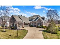 Beautiful stone home with a curved driveway and manicured lawn, accented with lovely trees under a bright blue sky at 16129 Brookhollow Dr, Westfield, IN 46062