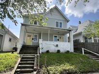 Charming two-story home featuring a welcoming porch and bright yellow doors, set against a backdrop of blue skies and lush greenery at 2148 Singleton St, Indianapolis, IN 46203