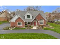 Charming brick home featuring a well-manicured lawn, mature trees, and a welcoming red front door at 643 Woodbine Dr, Carmel, IN 46033