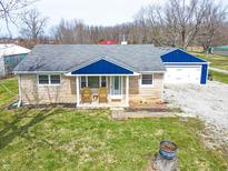 Quaint one story home with blue trim, a detached garage, and inviting front porch with chairs at 7212 E Rocklane Rd, Needham, IN 46162