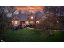 Stunning two-story brick home featuring a manicured lawn and mature landscaping under a dramatic, colorful sunset at 8939 Spider Bay Ct, Indianapolis, IN 46236