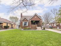 Charming brick home featuring a well-manicured lawn, landscaped garden beds, and a cozy covered front porch at 1139 N Butler Ave, Indianapolis, IN 46219