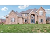A brick two-story home with a blue front door and arched entryway is nestled in a lush green yard at 10157 Woods Edge Dr, Fishers, IN 46037