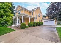 Inviting two-story home with yellow siding, a covered porch, and attached two car garage at 2353 Woodcreek Crossing Blvd, Avon, IN 46123