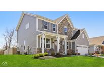 Two-story home featuring a welcoming front porch, stone accents, gray siding and lush lawn at 6557 Eagles Nest Ln, McCordsville, IN 46055