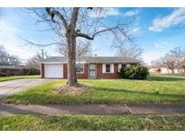 Charming brick home with an attached garage, green lawn, and a tree in the front yard at 4829 W 37Th St, Indianapolis, IN 46224