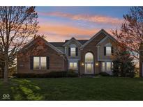 Charming two-story brick home with an arched entryway, manicured lawn, and mature trees under a vibrant sunset at 8965 Snowberry Ct, Zionsville, IN 46077