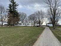 A manufactured home with white siding sits on a large lot with a gravel driveway and mature trees under a cloudy sky at 4653 E Us Highway 36, Markleville, IN 46056