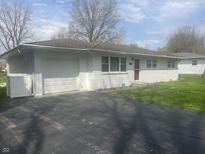 Charming one-story home with brick facade, attached garage, and driveway with a red front door at 7144 Lockwood Ln, Indianapolis, IN 46217