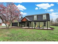 Beautiful home featuring green siding, black trim, lush lawn, mature trees, and a pergola-covered porch at 2103 Postmaster Ln, Greenfield, IN 46140