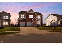 Beautiful two-story brick home with a two-car garage and manicured lawn, illuminated by the soft hues of twilight at 7128 English Oak Dr, McCordsville, IN 46055