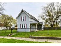 Charming two-story home featuring a fenced yard, covered porch, and traditional architecture with red shutters at 831 N 12Th St, Elwood, IN 46036